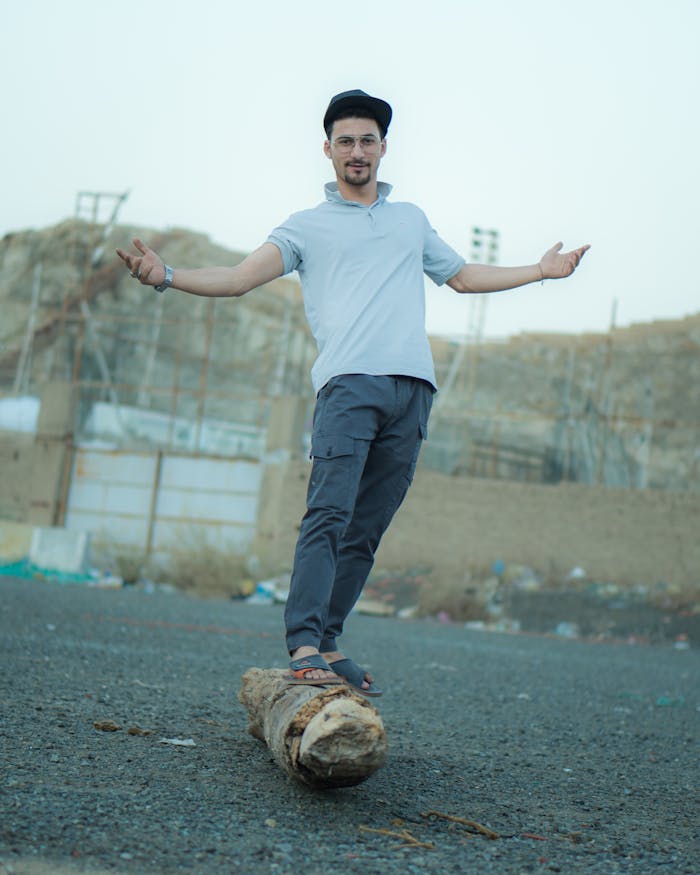 Casually dressed man balancing on a log at a construction site, showcasing an urban style.