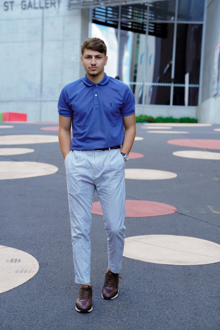Stylish man with hands in pockets stands on a street with distinctive patterned pavement.